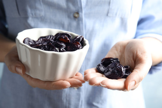Woman holding bowl and handful of dried plums, closeup. Healthy fruit