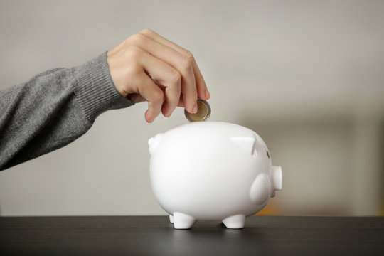Even adults are allowed to have piggy banks, Woman putting a coin in a white piggy bank, starting with savings concept