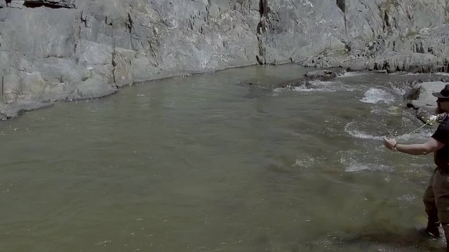 A slow motion shot of a fly fisherman casting while standing in a roaring river.