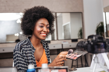 Cute dark-skinned woman with coral lipstick conducting online tutorial - obrazy, fototapety, plakaty