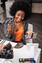 Pretty dark-skinned woman with coral lipstick holding blusher palette