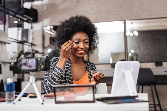 Smiling dark-skinned woman in an orange top showing how to correct eyebrows