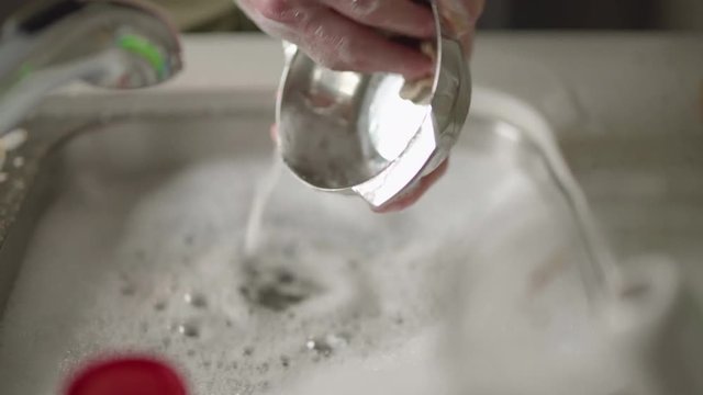 Dolly across kitchen sink as man's hands clean a shiny silver bowl in dishwater