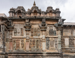 Fototapeta na wymiar Belur, Karnataka, India - November 2, 2013: Chennakeshava Temple . Large Brown wall stone side panel sculpture of many idols each on their pedestals. White sky.