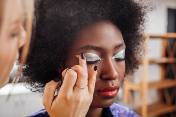Fair-haired young stylist with black nail polish putting eyeshadows