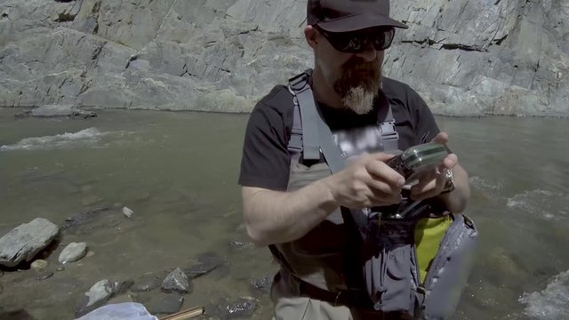 A fly fisherman selects a fly from his pack.