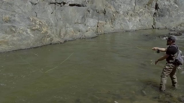 A slow motion shot of a fly fisherman standing in a roaring river while casting and mending line.
