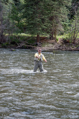 Angler flyfishing in Colorado river wearing gray waders and yellow shirt.