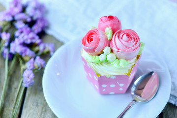 Vanilla cup cake and spoon on a plate with cup cake in background and flower  as decoration for...