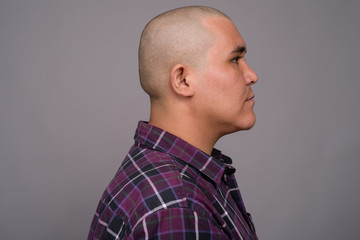 Young bald Asian businessman against gray background