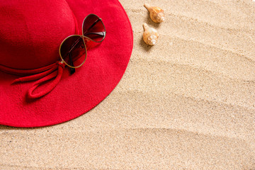 red hat on sandy beach with sunglasses, seashells and copy space for text.