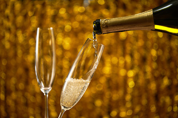 Pouring champagne into glass on golden stylish background with golden bokeh circles place for text