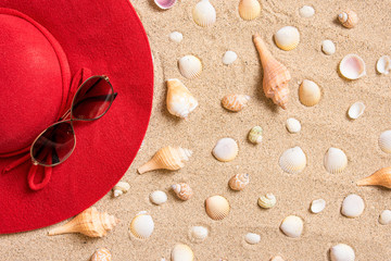 Fototapeta na wymiar red hat on sandy beach with sunglasses, seashells and copy space for text.