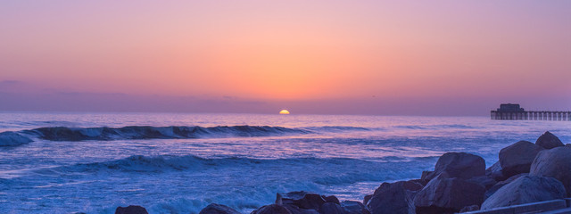 Pink and purple beach sunset over rocky edge of road