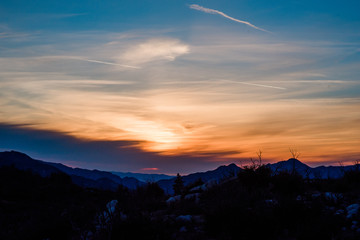 Obraz premium Wispy glowy orange and peach sunset over blue ridges in California mountains