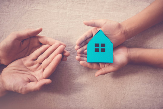 Adult and child hands holding white house, family home and homeless shelter concept