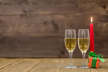 Pair glass of champagne and gift box with candle. Wooden background with empty space for text