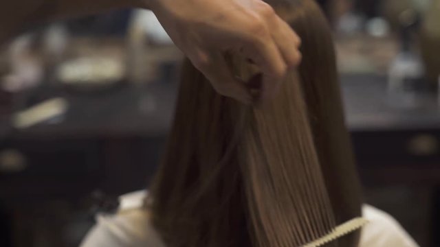 Hairstylist cutting hair of brunette woman with scissors in hairdressing salon. Woman haircut concept. Hairdresser using barber scissors and comb for female haircut. Beauty and hairstyling.
