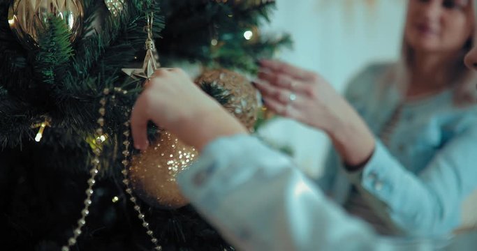 Mom and daughter decorate the Christmas tree. Girl hangs a ball on a branch of spruce. Close-up.