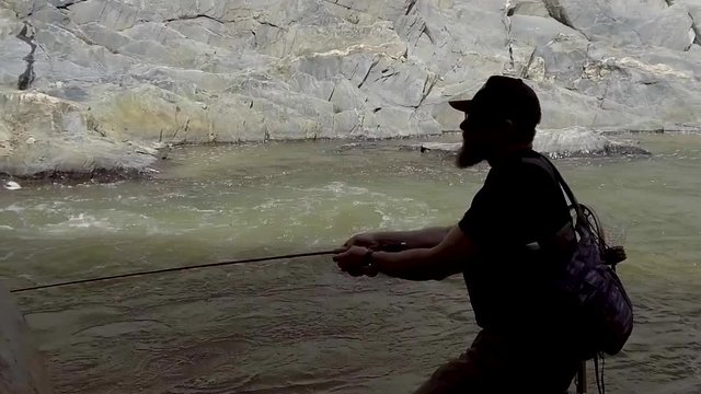 A fly fisherman is nicely silhouetted as he casts and mends in slow motion while standing in a roaring river.