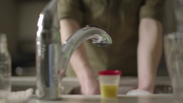 Dolly across kitchen counter as man cleans clear plastic cup in dishwater