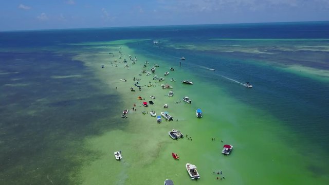 AERIAL: wide push with a final tilt down over a strip of sand bar, off the coast of souther Florida, that's loaded with people and boats.
