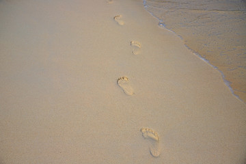 Yellow sand beach with foot step marks and seawater. Lonely traveler barefoot steps. Still seawater on sand beach