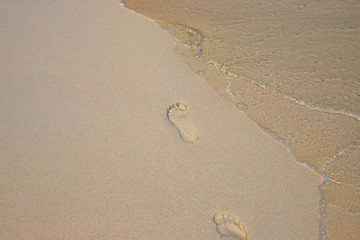 Bare foot step mark on sand beach by sea water tide. Lonely traveler barefoot steps. Clear seawater on sand beach