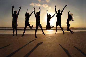 group of young people jumping on a beach with hands up on sunset
