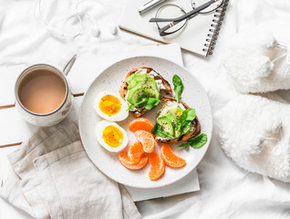 Womens cozy breakfast in bed still life - coffee, avocado sandwiches, boiled egg and tangerine on a light background, top view. Morning inspiration plan