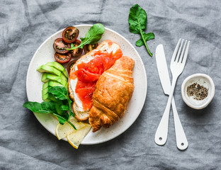 Croissant with cream cheese and smoked salmon, avocado and cherry tomatoes delicious - balanced breakfast, brunch or snack on a grey background, top view