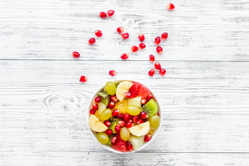 Fruit diet concept. Fruit salad with apple, kiwi and pomegranate in bowl on white wooden background top view copy space