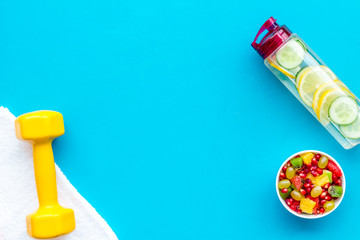 Healthy lifestyle, healthy habits. Detox water, fruit salad, sport equipment dumbbells on blue background top view copy space