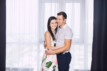 Beautiful young couple in love man and woman in a room together in front of a window