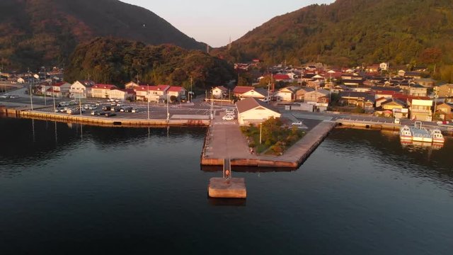Aerial pull back as sun sets over beautiful Oki Island port as sunsets over small towns Japanese homes.