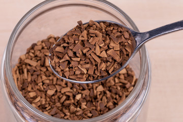Instant coffee in a spoon.Close up.Glass transparent jar with coffee granules. View from above.