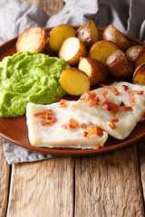 Rustic style Lutefisk with pea puree, baked potatoes and bacon close-up on a plate. vertical