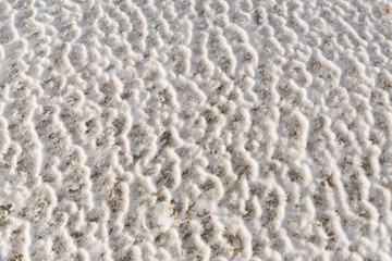 Frozen wavy texture of snow strewn with sand and mud.