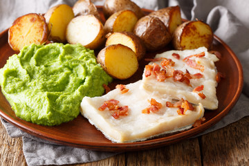Cod Lutefisk with pea puree, baked potatoes and bacon close-up on a plate on the table. horizontal