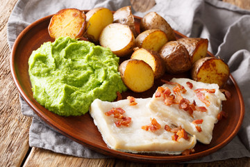 Norwegian cod lutefisk served with pea puree, potatoes and bacon close-up. horizontal