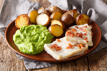 Traditional Scandinavian dish lutefisk served with pea puree, potatoes and bacon close-up....