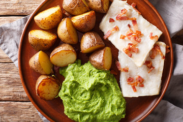 Organic codfish Lutefisk with pea puree, baked potatoes and bacon close-up on a plate. Horizontal...