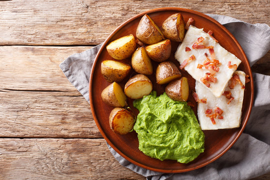 Popular Scandinavian food Lutefisk from cod with pea puree, baked potatoes and bacon close-up on a plate. Horizontal top view