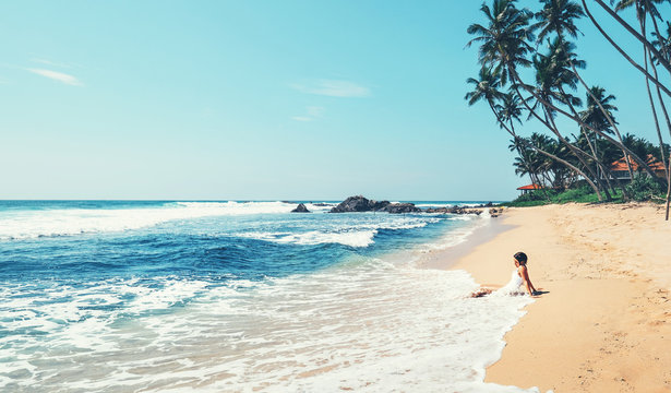 Woman enjoy with ocean surf sitting on the lonely tropical beach under the palm trees