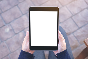 Top view mockup image of a woman holding black tablet pc with blank white screen while sitting in the outdoors