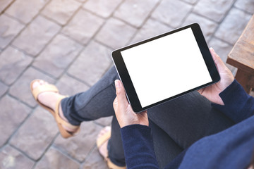 Mockup image of a woman holding black tablet pc with blank white screen horizontally while sitting in the outdoors