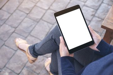 Mockup image of a woman holding black tablet pc with blank white screen while sitting in the outdoors