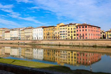 Fototapeta na wymiar Colorful houses are reflected in the water of arno river under clear sky in Pisa, Tuscany, Italy