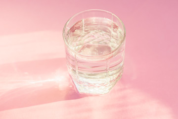 Close up of sparkling water in transparent glass and sun glare on pink background.