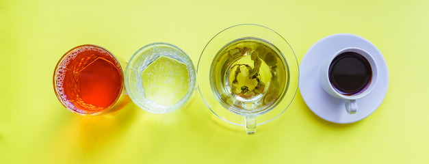 Top view of different beverages - drinking coffe, sparkling water, apple juice and green tea on yellow backgeound. Healthy life and diet concept
